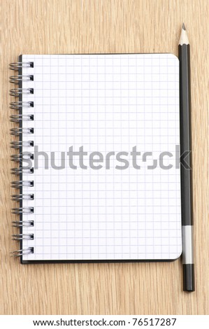 Spiral notepad with blank page and pencil on wooden desk. View from above.