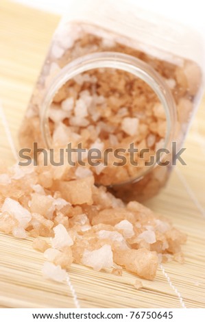 Peach-colored bath salt spilled of jar on mat. Focus on foreground.