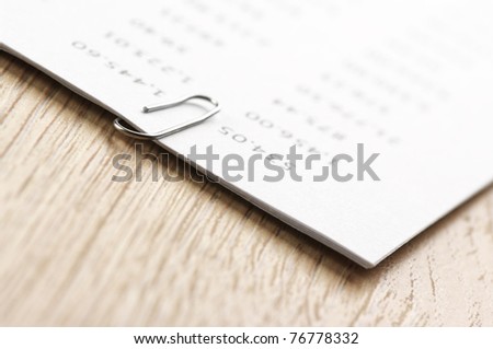 Close-up of pages fastened with paper clip on wooden desk.