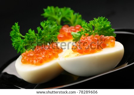 Canapes with egg, salmon caviar and parsley on black plate against dark background..