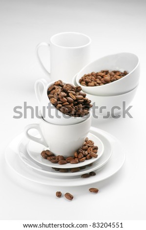 White tableware with roasted coffee beans on light background.