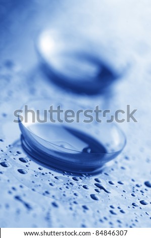 Close-up of two contact lenses with drops on light background. Blue toned image.