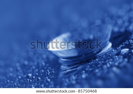 Close-up of contact lens with drops on dark background. Blue toned image.