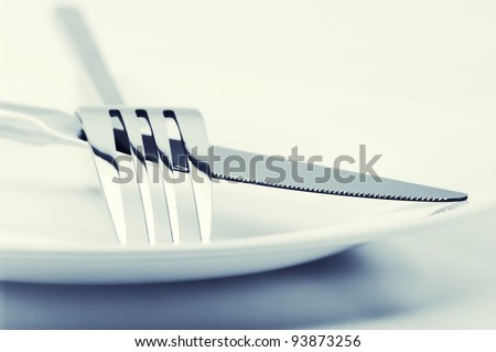 White plate, fork and knife on light background. Toned image.