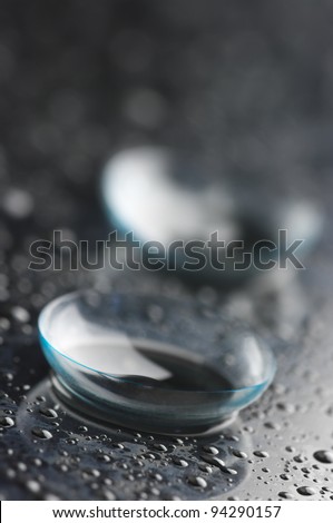 Close-up of contact lens with drops on dark background.