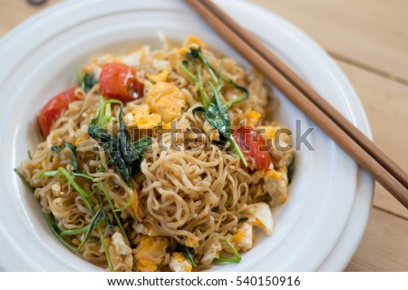 Close up fried instant noodle with egg and mix vegetable in the plate on the table.