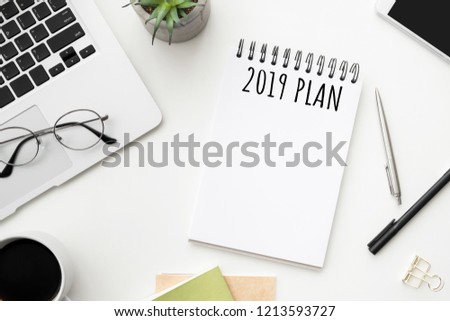 Notebook page with 2019 plan text on white office desk table. Top view, flatl lay.
