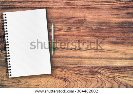 A blank notebook page and pen on wood office table. Top view with copy space.