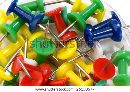Multicolored push pins in transparent box close-up on white background