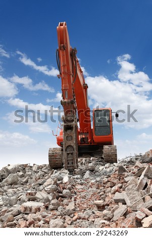 An excavator with a hydraulic hammer attachment in a destruction area.