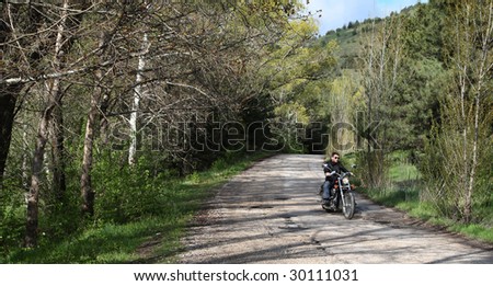 Young rider driving his cruiser-type motorcycle on the forest road.