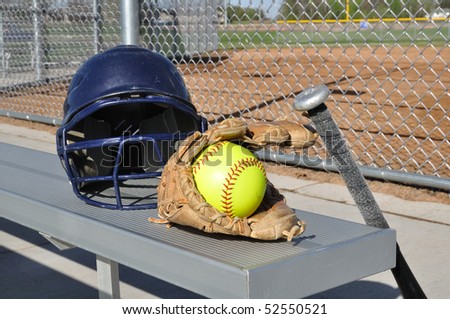 Yellow Softball, Helmet, Bat, and Glove on an Aluminum Bench