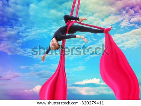 Active smiling sportive cheerful child training dancing performing on aerial silks or ribbons, hanging upside down in the blue rainbow sky Childhood, sports, happiness, active lifestyle concept.