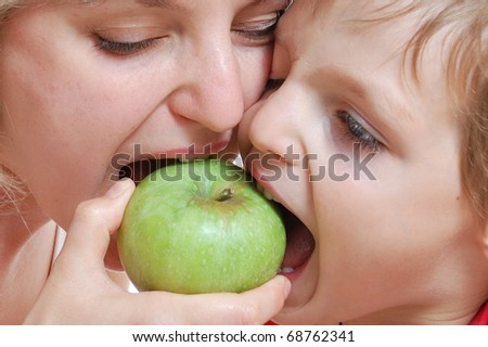 portrait of mother and son biting a green apple