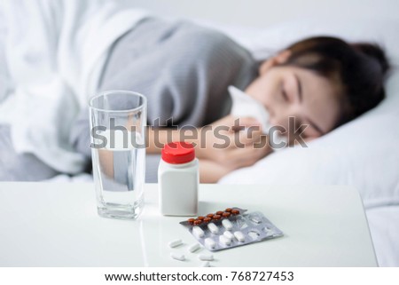 Sick woman covered with a blanket lying in bed with high fever and a flu, resting. Teapot, pills and lemon on the table