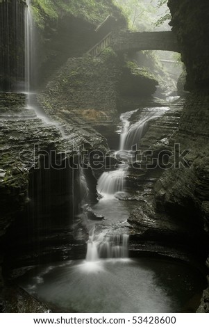 stone bridge with two waterfalls in gorge with misty rain