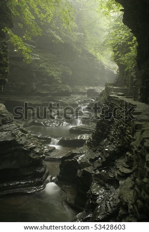 waterfall in gorge with misty rain and sunlight showing through the trees