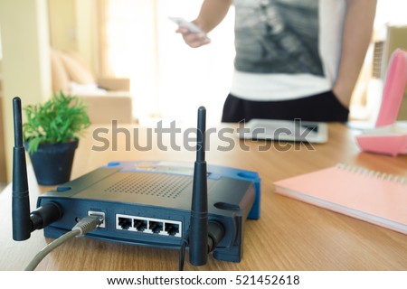 closeup of a wireless router and a young man using a smartphone  on living room at home with a window in the background