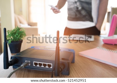 closeup of a wireless router and a young man using a smartphone  on living room at home with a window in the background
