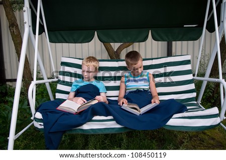 8-year old schoolboy and 6-year old preschooler reading books on garden swing outdoors