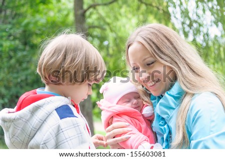 Young mother with her kids in the forest. Son is jealous mum of younger sister.