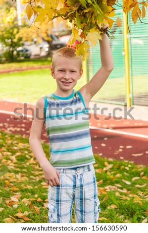 Adorable boy smiling and holding autumn leaves at school yard