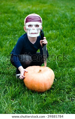 young boy wearing skull mask attacking halloween pumpkin