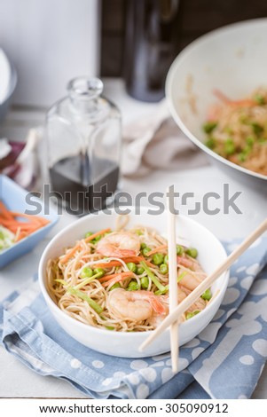 Chow mein with shrimps in white bowl with soy sauce, greens and carrot