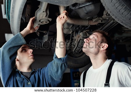Two mechanics repairing car in garage under the car.