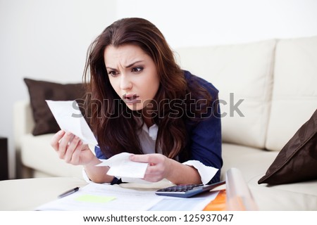 Desperate young woman calculating bills in living room