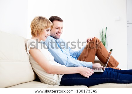 Happy young couple sitting on couch using laptop