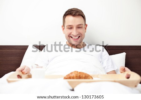 Happy single man eating breakfast in bed