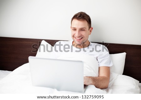 Happy young man sitting in bed with his computer