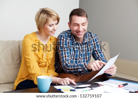 Happy couple calculating bills sitting sonf sofa in living room