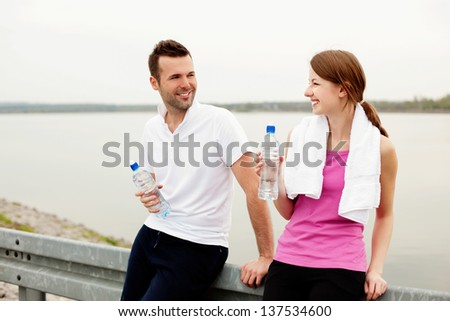 Happy woman and man talking and drinking water after exercise