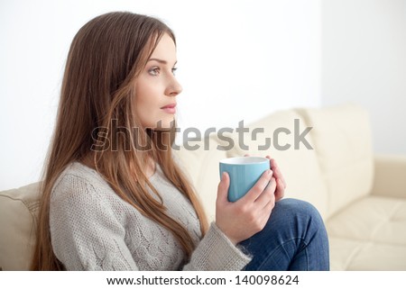 Sad woman sitting on couch with cup looking ahead