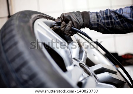 Tire pressure check. Closeup of mechanic inflating tyre with alloy wheel