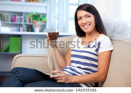 Happy woman on couch with caffee and digital tablet