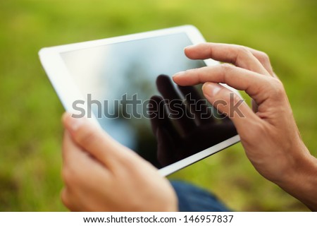 Close-up of digital tablet used by woman in park. Grass in background