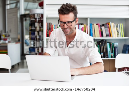 Happy man working on laptop in library