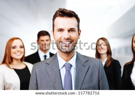 Portrait Of Happy Team Leader With Group Of Business People In Background