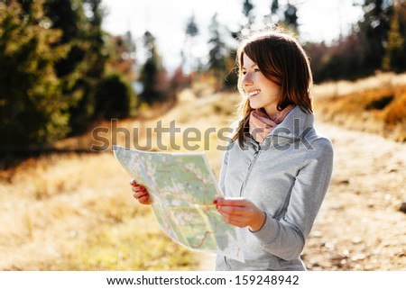 Happy woman reading map on trial during autumn in mountains