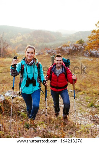 Happy couple hiking with backpacks and sticks in mountains