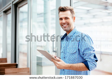 Happy young man smiling into the camera with a tablet in his hand