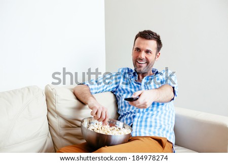 Young smiling man changing channels with a remote control