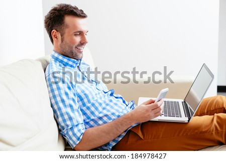 Smiling young man using his mobile and a laptop