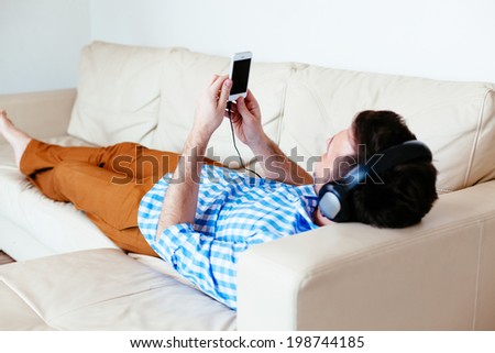 Young man relaxing on a sofa and listening to music on his smartphone