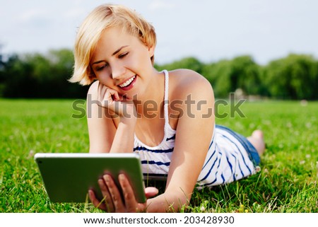 Portrait of a young blond lady lying on the grass and using a tablet