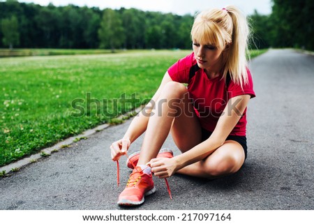 Photo of a female jogger sitting on the ground and lacing up her running shoes