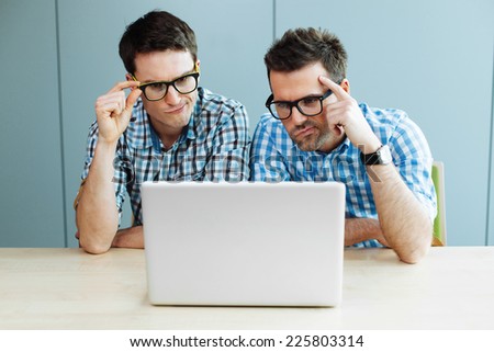 Two unhappy computer geeks working on laptop in office